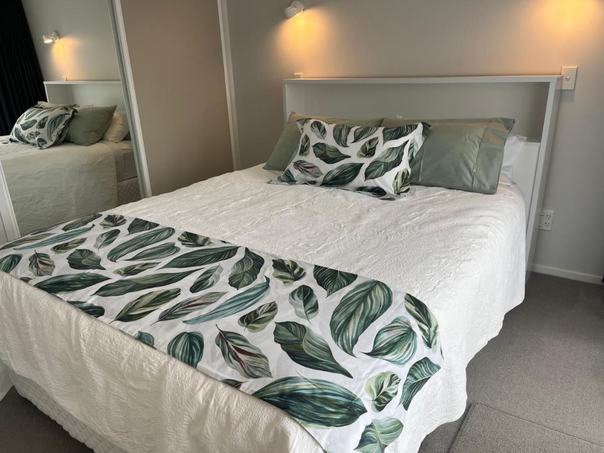 The queen bed with white quilt and green leaf-print runner, reading lights on