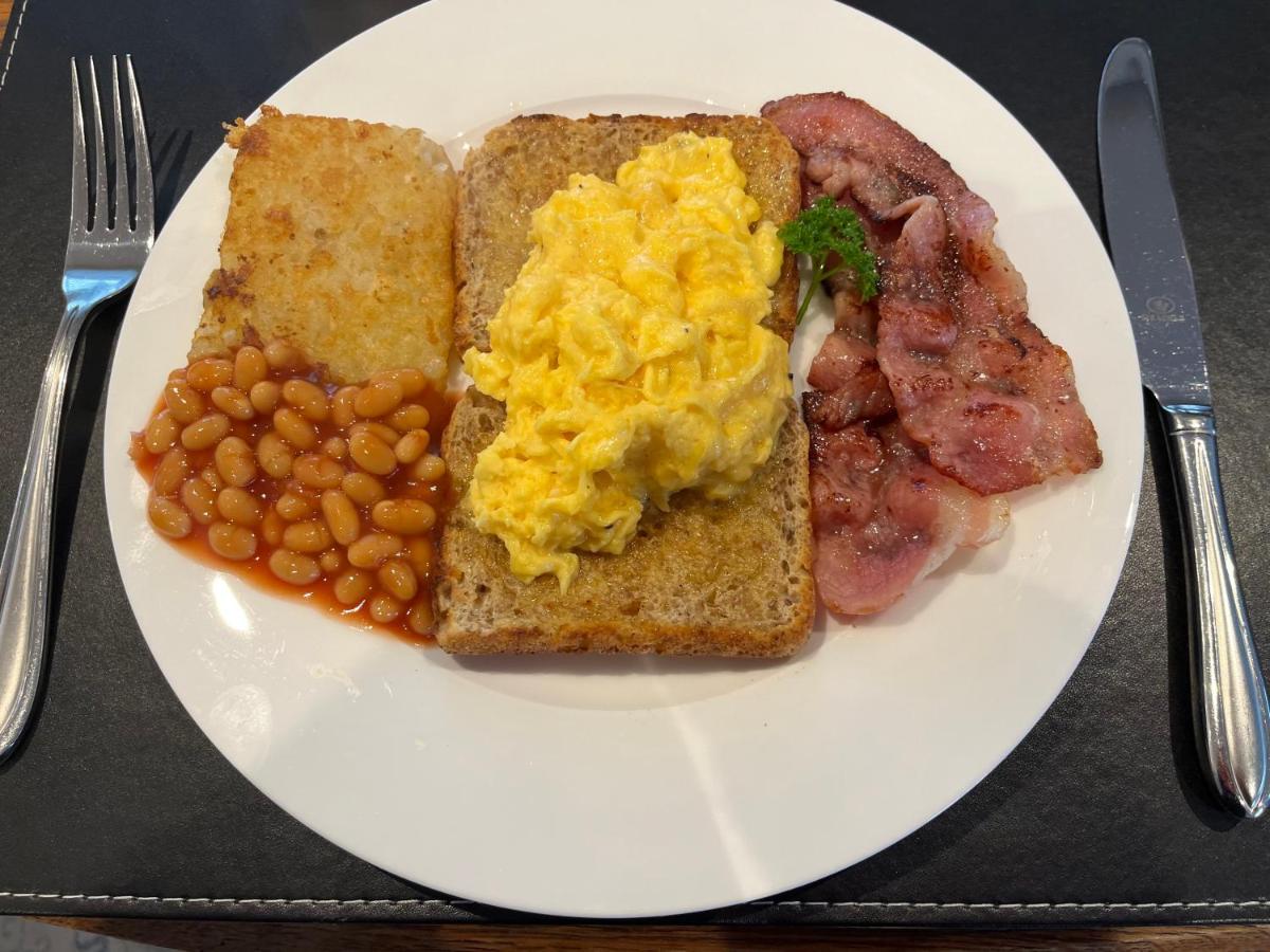 A cooked breakfast — scrambled eggs on toast with bacon, hash brown and baked beans