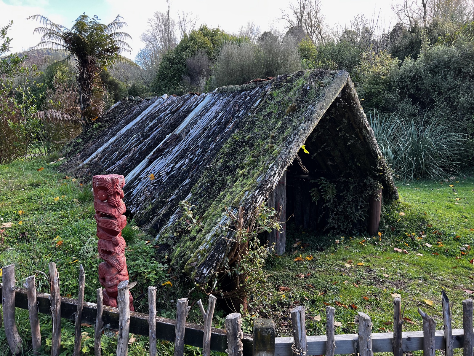 A whare with red carved pou at the excavated Buried Village site today, among tree ferns
